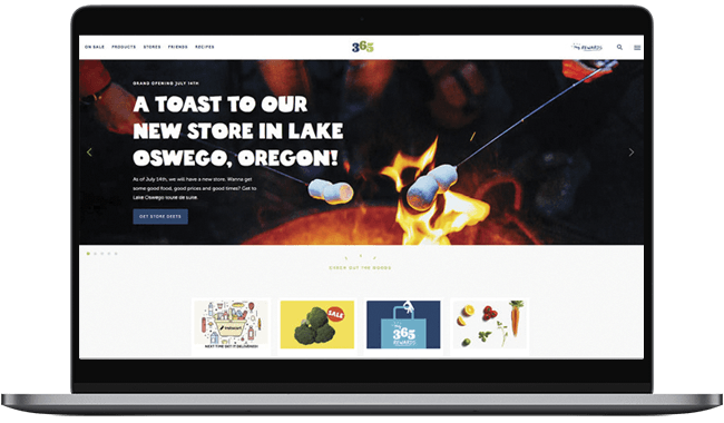 Homepage of a grocery store website announcing the opening of a new location in Lake Oswego, Oregon, featuring vibrant visuals of food items and a campfire theme.
