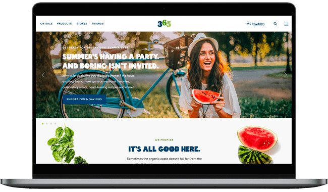 Laptop displaying a vibrant summer-themed webpage for 365, featuring a smiling woman holding a slice of watermelon, with a bicycle in the background and promotional text about summer fun and savings.