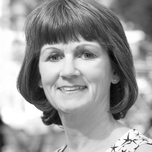 Smiling woman with short brown hair and a floral patterned top, posed outdoors in a blurred background.