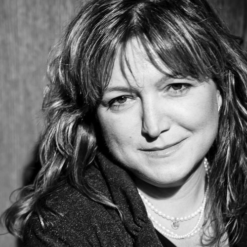 Black and white portrait of a woman with wavy hair, smiling softly at the camera, conveying a warm and approachable demeanor.