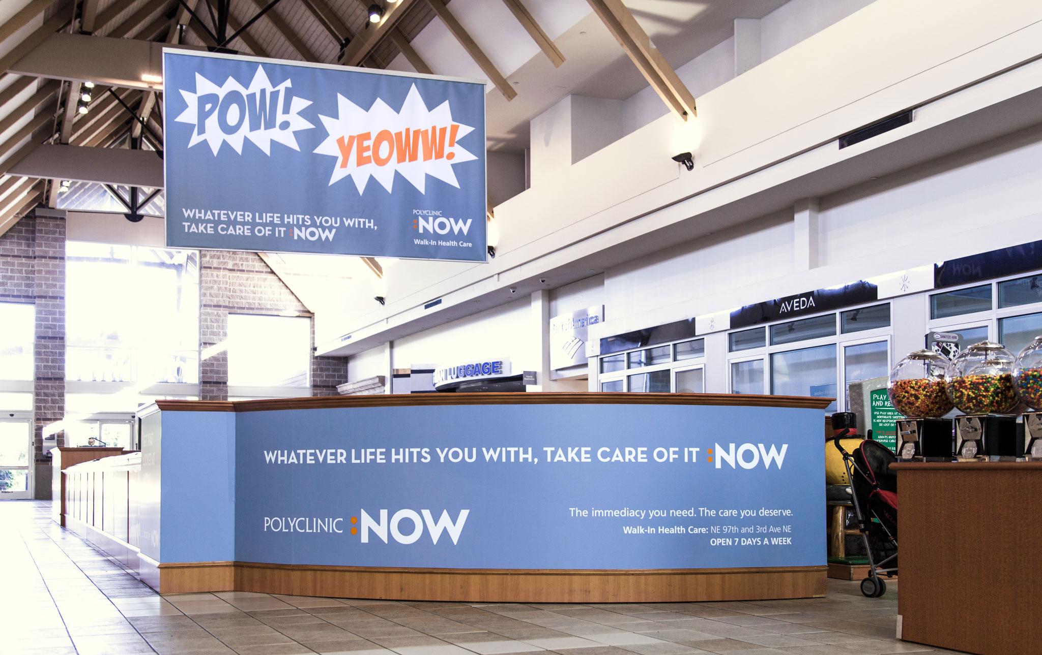 Informative marketing display in a modern retail space featuring bold graphics with phrases "POW!" and "YOW!" promoting a service. The counter showcases the brand name "NOW" and emphasizes customer care with the message "Whatever life hits you with, take care of it NOW."