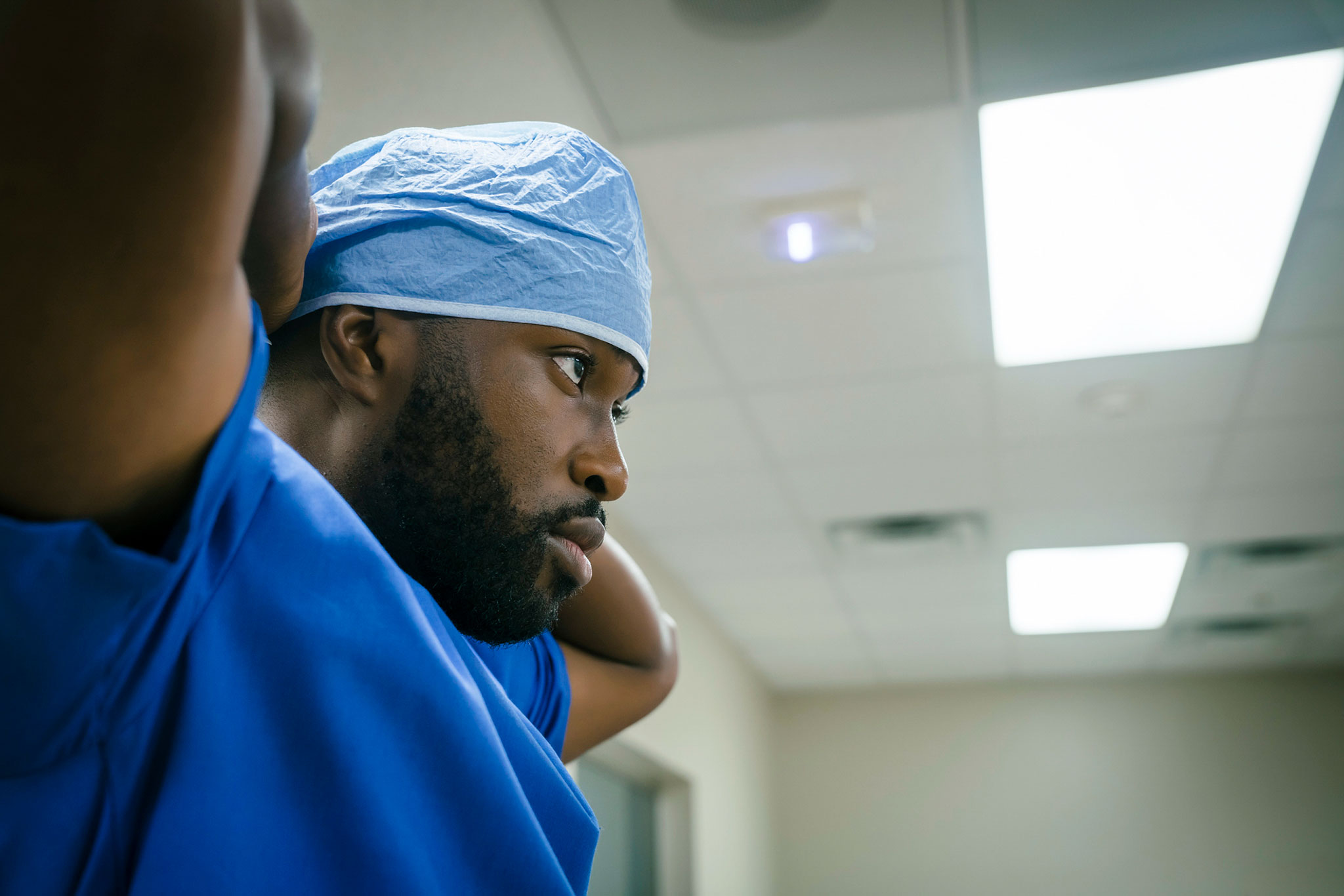 Surgeon in blue scrubs and surgical cap preparing for a procedure, focusing intently in a well-lit hospital environment.