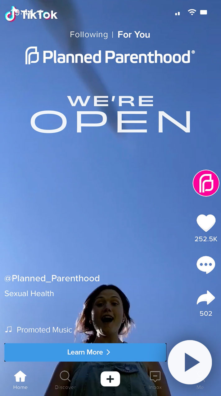 TikTok video from Planned Parenthood featuring the text "We're Open," promoting sexual health services. The video showcases a smiling woman against a blue sky, encouraging viewers to learn more about available resources.