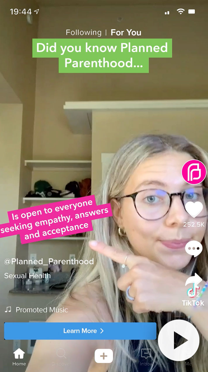 A young woman with glasses points to text about Planned Parenthood, emphasizing its openness to those seeking empathy, answers, and acceptance. The background features a closet, and the image includes social media elements, highlighting the topic of sexual health.