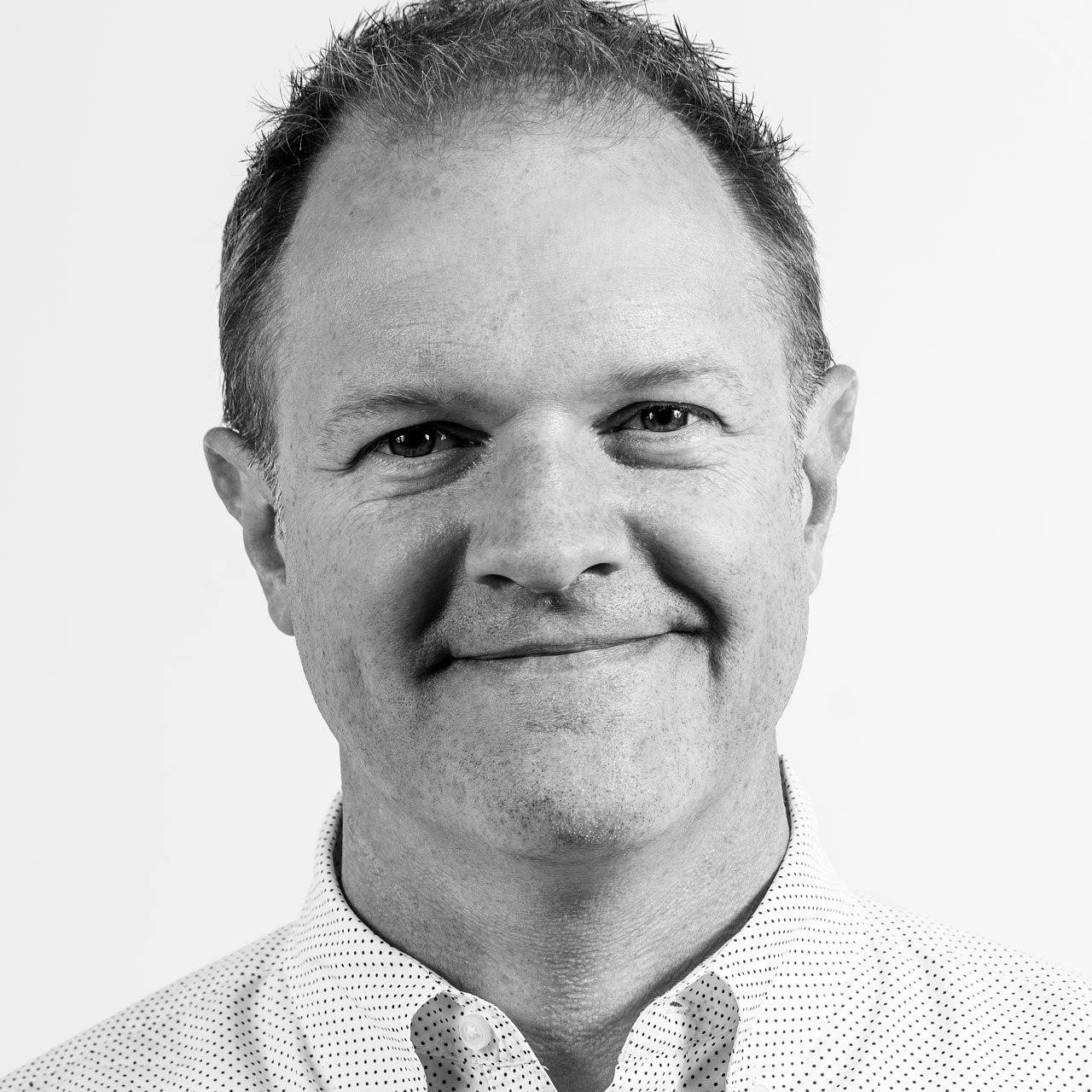Professional headshot of a smiling man with short hair, wearing a collared shirt, against a plain background.