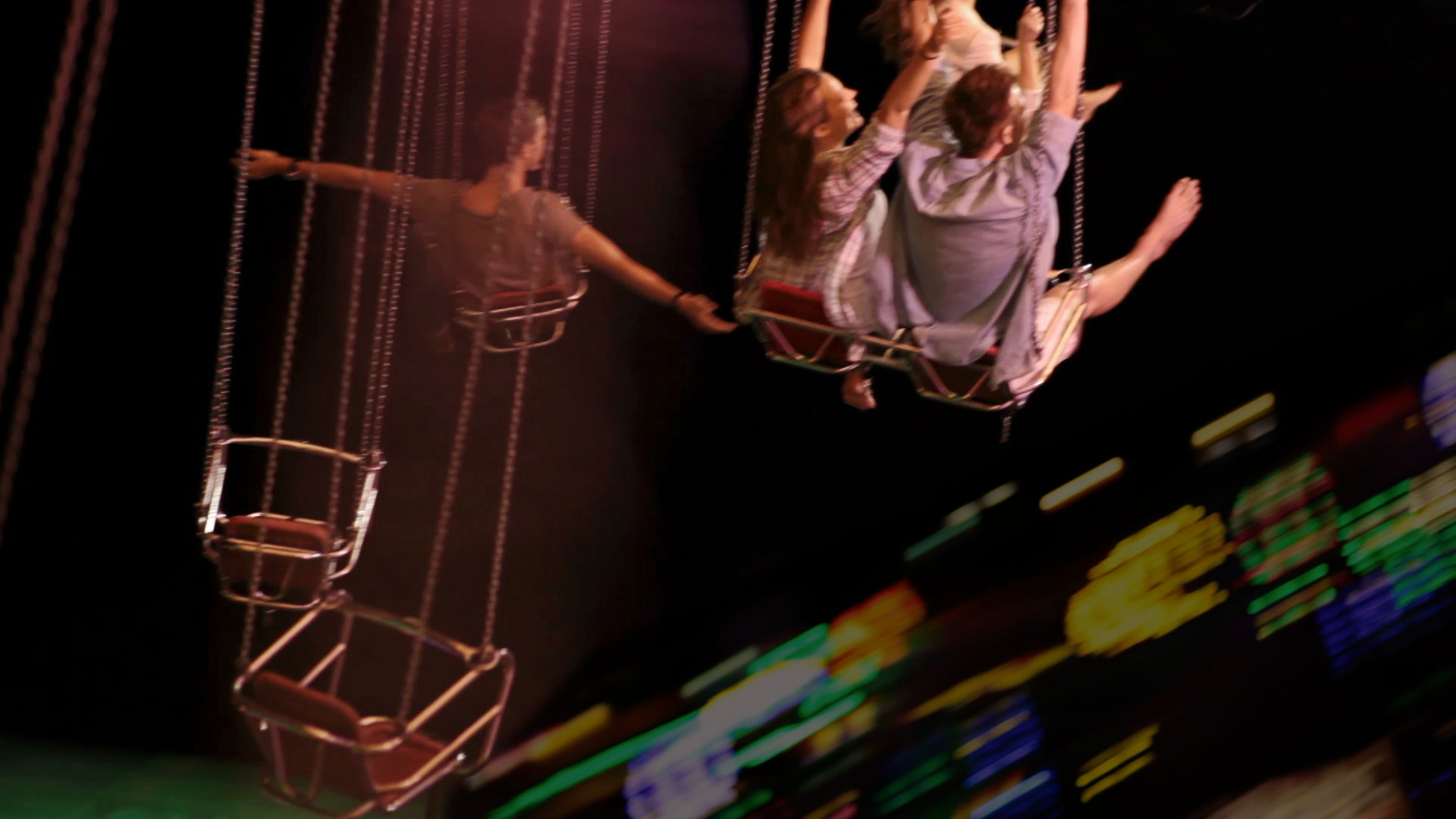 A group of people enjoying a night ride on a spinning swing attraction at a fair, with vibrant lights creating a colorful backdrop.