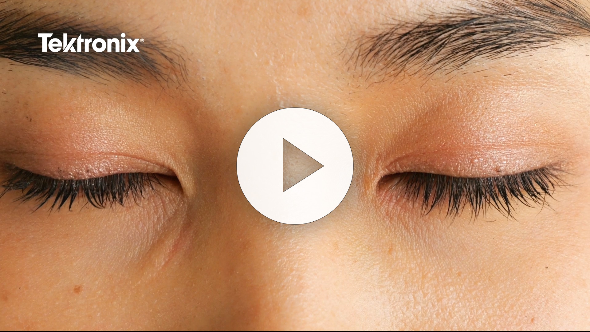 Close-up image of closed eyes with long eyelashes, highlighting skin texture. A play button is overlaid in the center, indicating video content related to eye care or beauty. Tektronix logo is visible in the top left corner.