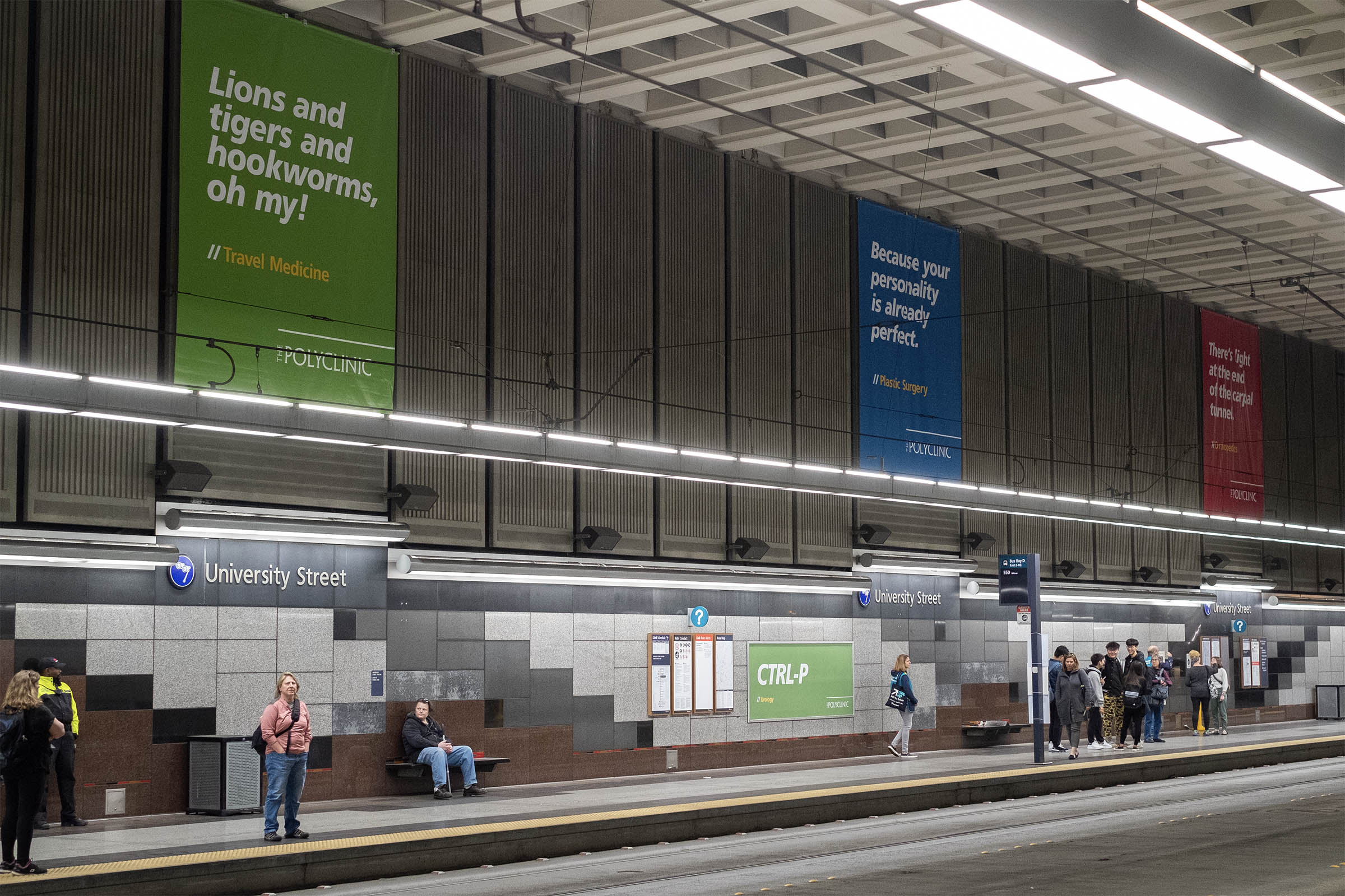 Interior view of a modern subway station featuring passengers waiting on the platform, digital schedule displays, and colorful advertisements on the walls promoting various services.