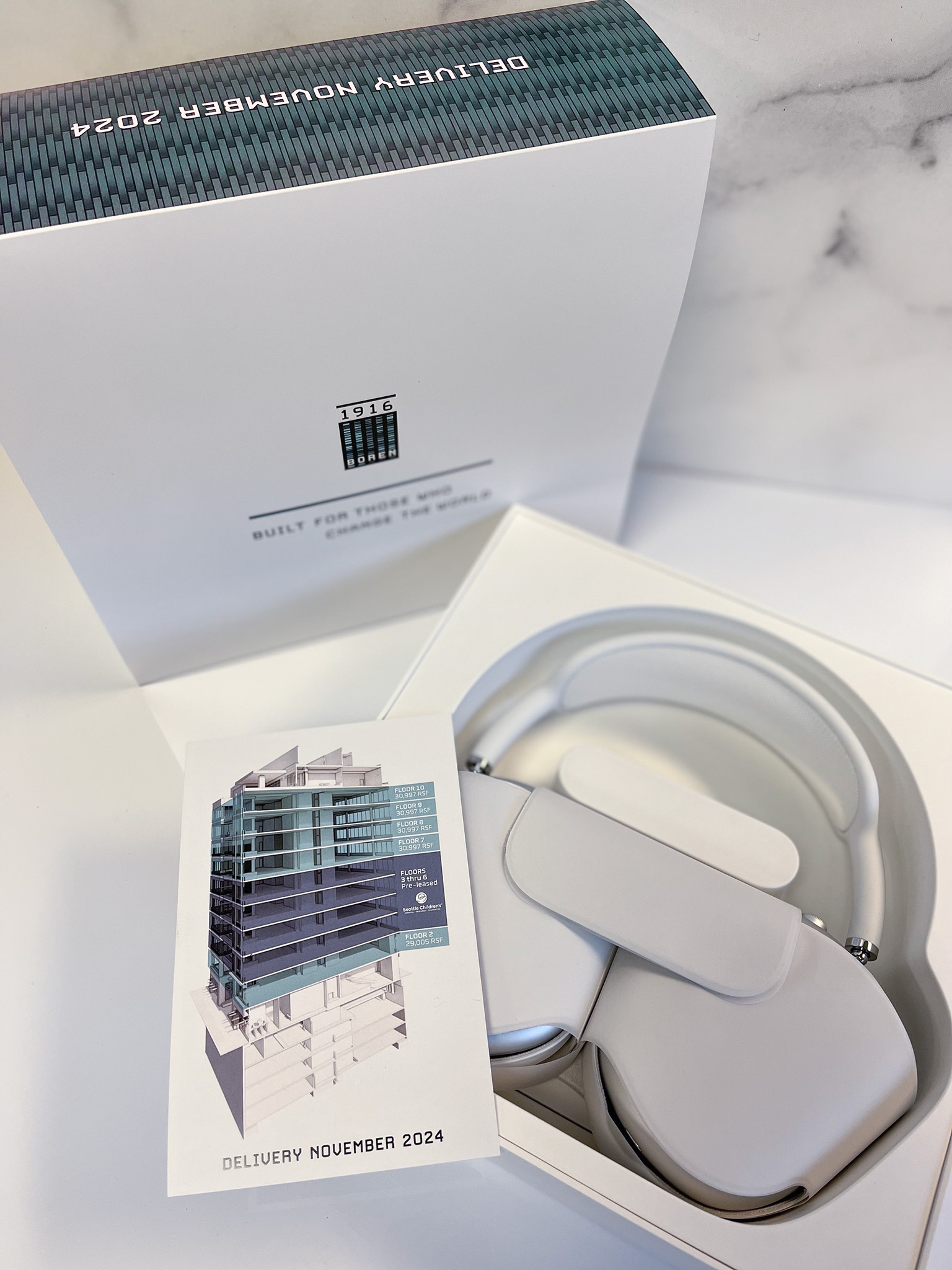 Wireless headphones displayed in an elegant packaging with a sleek design, showcasing a modern aesthetic and a promotional card featuring an architectural image.
