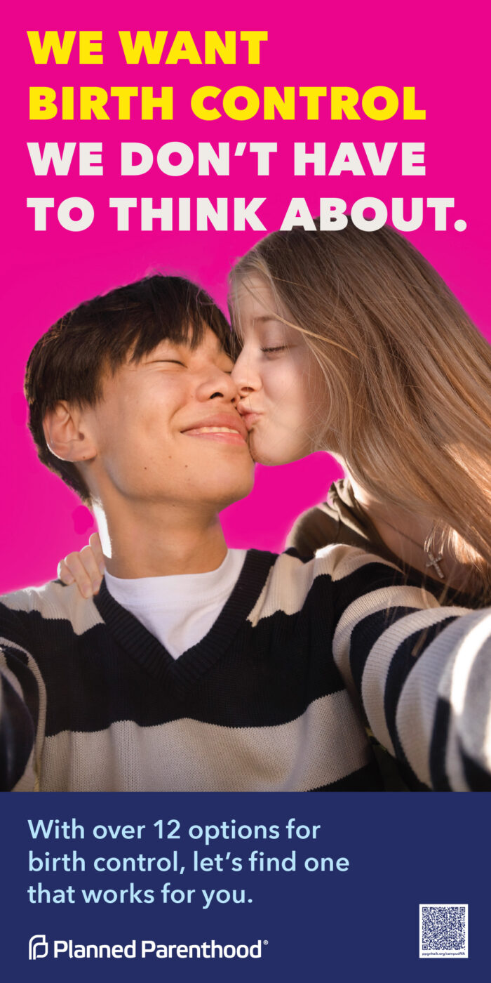 Young couple smiling and sharing a kiss in front of a vibrant pink background, capturing a moment of affection and happiness.