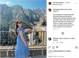 Woman in a blue dress standing on a balcony with a scenic mountain backdrop, enjoying the view in a sunny location.