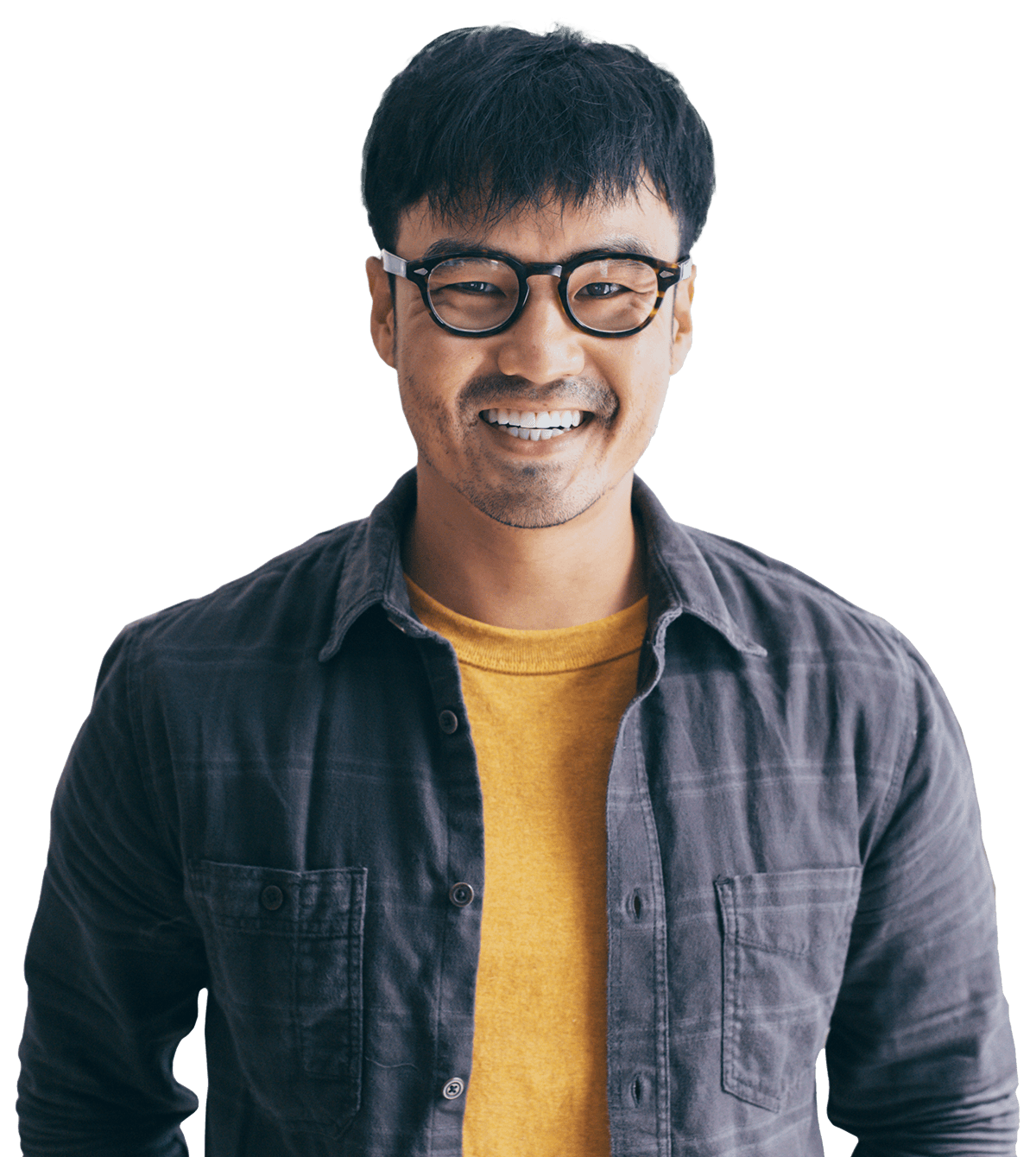 Smiling man with glasses wearing a dark shirt over a yellow sweater, standing against a transparent background.
