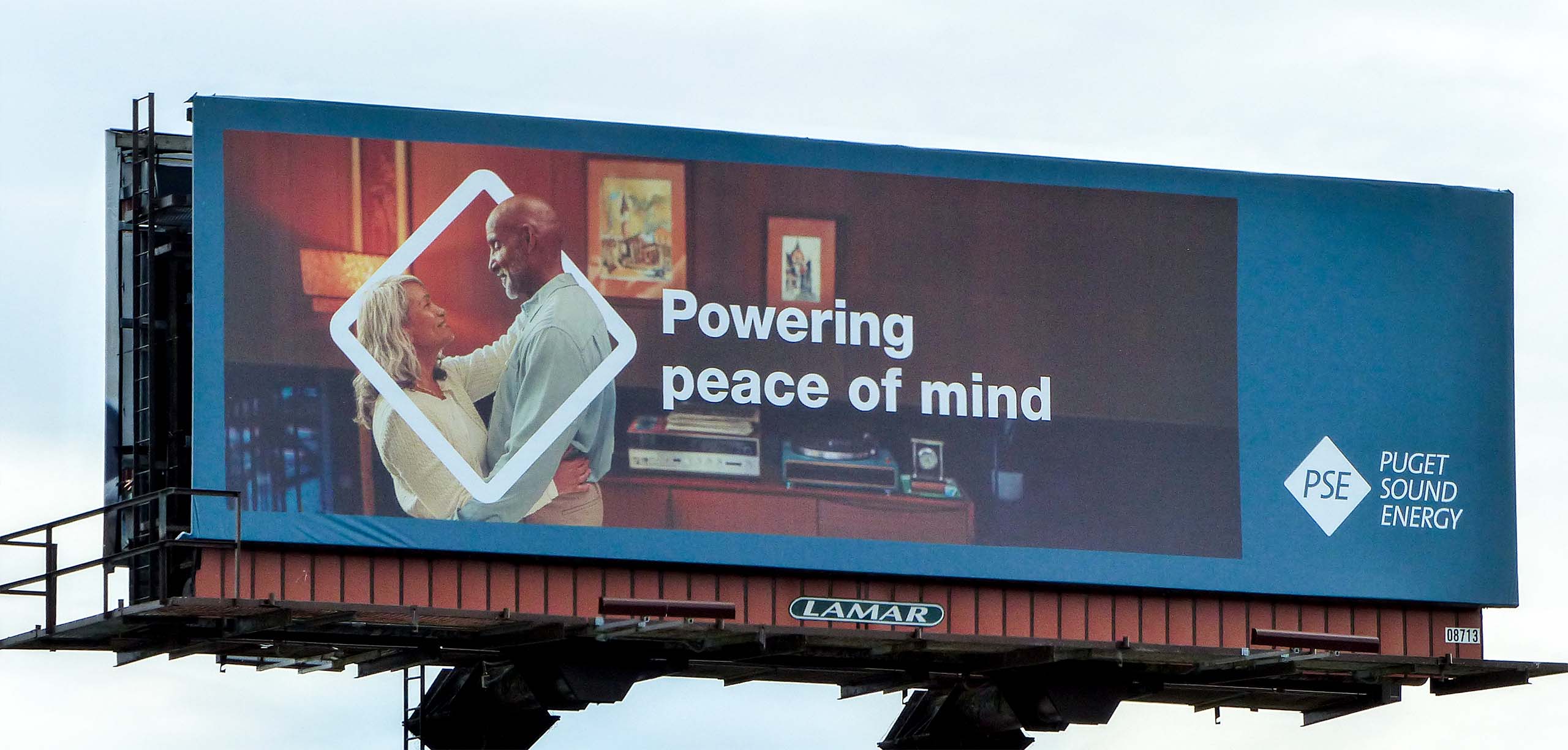 Billboard featuring a happy couple embracing, promoting a message about "Powering peace of mind." The background includes a cozy interior setting, emphasizing warmth and connection.
