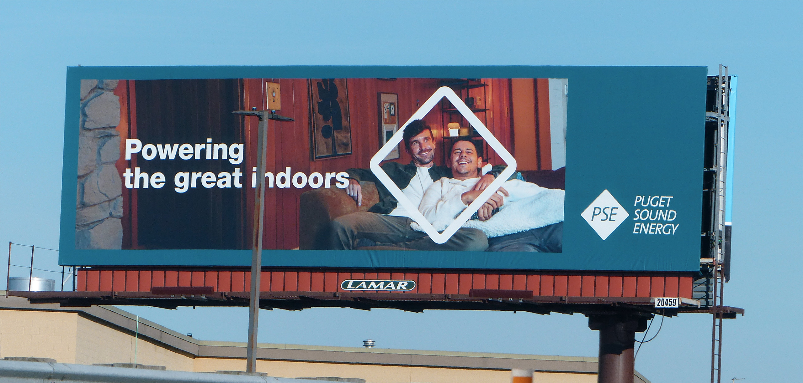 Billboard promoting indoor heating, featuring two smiling men cozying up on a couch with a blanket, emphasizing comfort and warmth during colder months.