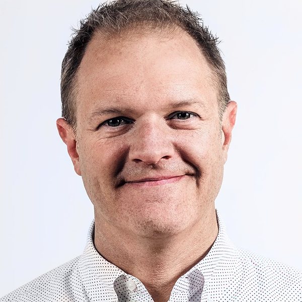 Smiling middle-aged man wearing a white button-up shirt with a subtle pattern, against a plain white background, conveying professionalism and approachability.